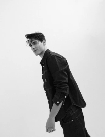 Model Iasonas Laios wearing a dark denim button-down shirt and matching jeans against a plain white studio background.