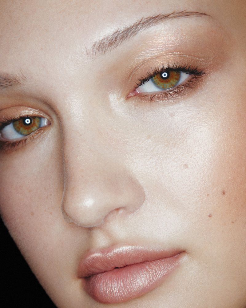 Close-up portrait of a woman with bronze eyeshadow, healthy skin, and glossy lips, capturing the detail of her features in soft lighting.