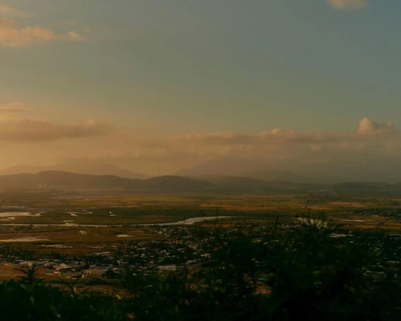 Scenic vista of a green valley landscape with meandering rivers, low mountains in the distance under a partly cloudy sky during golden hour.