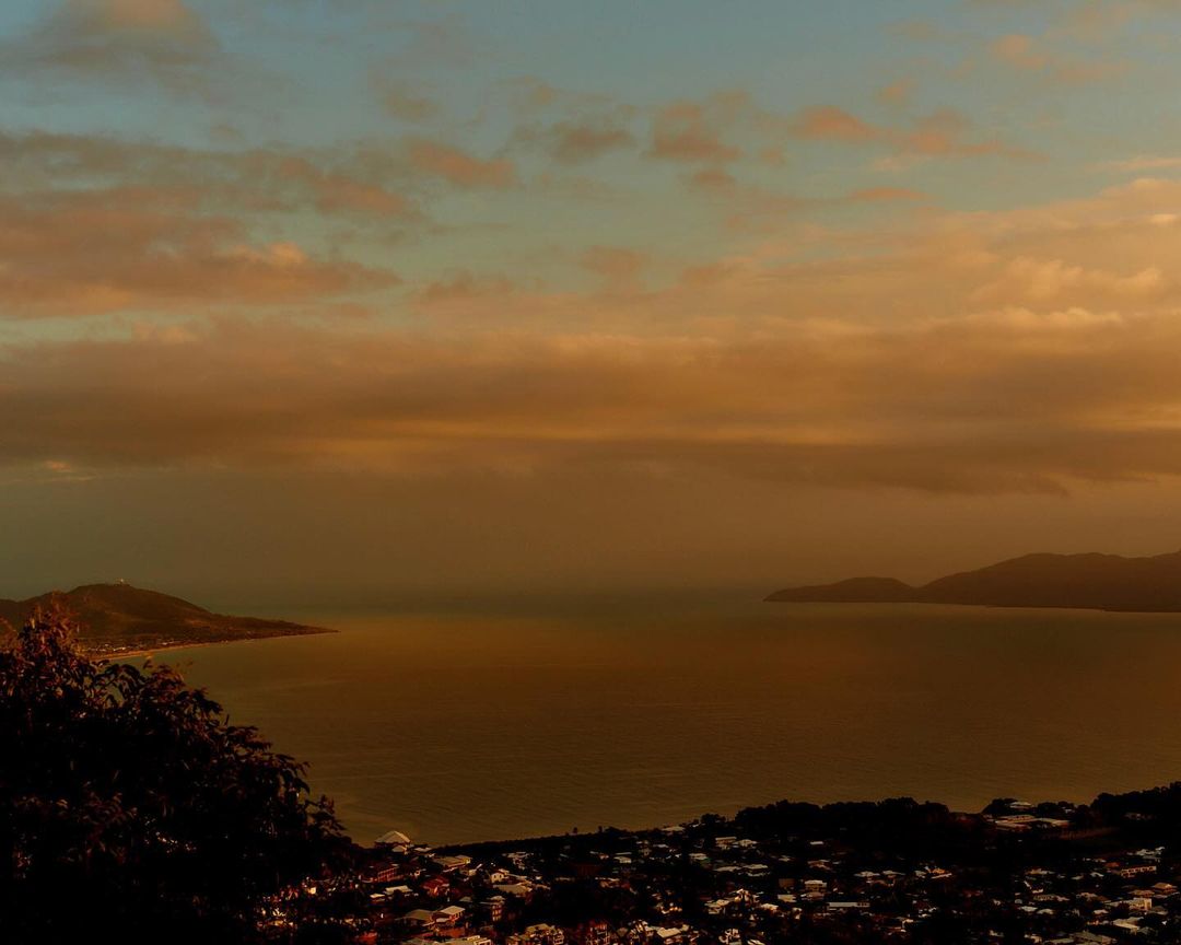 Wide shot of calm sea with mountains and a cloudy sky during a golden hour, showcasing the natural beauty and serene atmosphere.