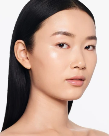 Close-up studio shot of a young Asian woman with fair skin, dark hair, and natural makeup, posing against a plain white backdrop.