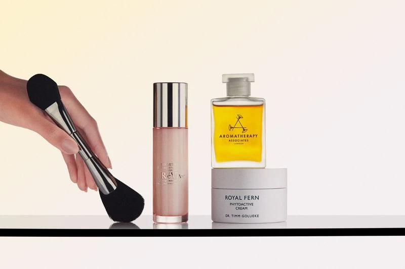 Cosmetic product arrangement featuring a makeup brush, skincare serum, oil, and cream on a white surface, ideal for beauty campaigns.