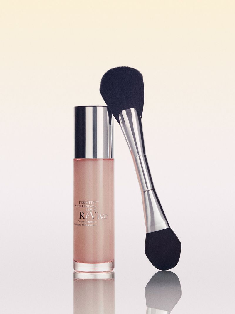Cosmetic bottle and brush set. ReVive skincare bottle and a make-up brush are isolated on a white surface with gradient background.