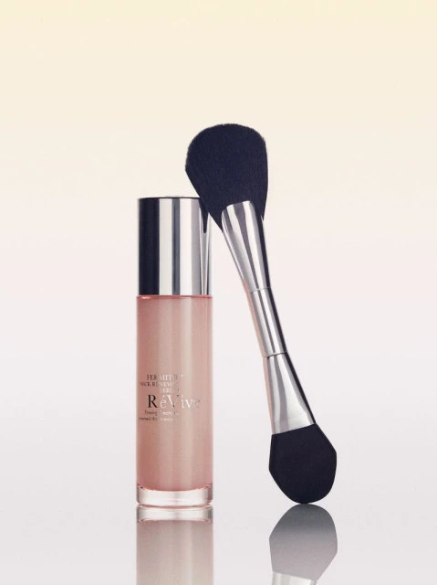 Cosmetic bottle and brush set. ReVive skincare bottle and a make-up brush are isolated on a white surface with gradient background.