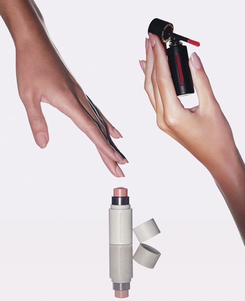 Product shot featuring hands holding makeup and a reflection of the items on a white background, with two hands in frame.