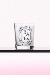 Diptyque Baies scented candle in a clear glass jar on a black shelf against a pale gradient background.
