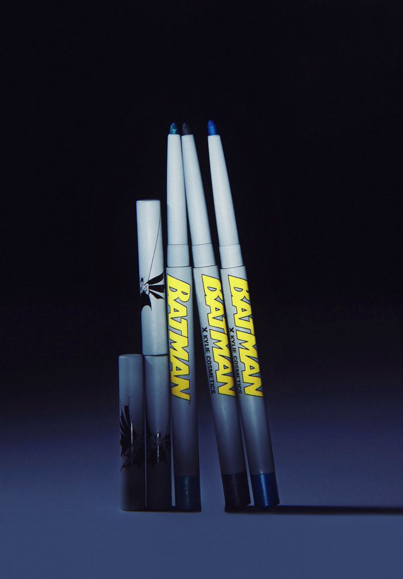 Cosmetic eyeliner set with 'Batman' branding in cool tones. Three pencils with graphic covers sit against a dark backdrop.