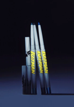 Cosmetic eyeliner set with 'Batman' branding in cool tones. Three pencils with graphic covers sit against a dark backdrop.