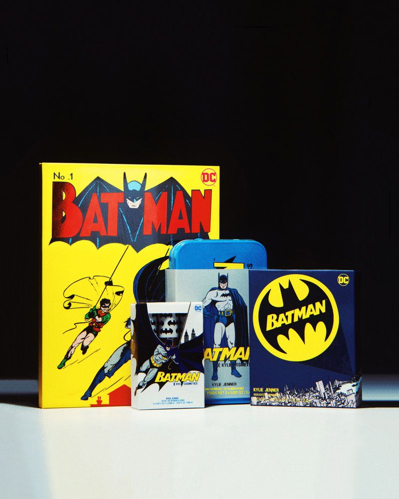 A collection of Batman comic books and merchandise, including a yellow-covered comic book, arranged on a white surface against a black background.