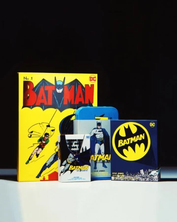 A collection of Batman comic books and merchandise, including a yellow-covered comic book, arranged on a white surface against a black background.