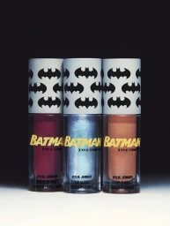 Three Kylie Cosmetics Batman collection lip gloss and lip paint tubes arranged in a row against a dark background.