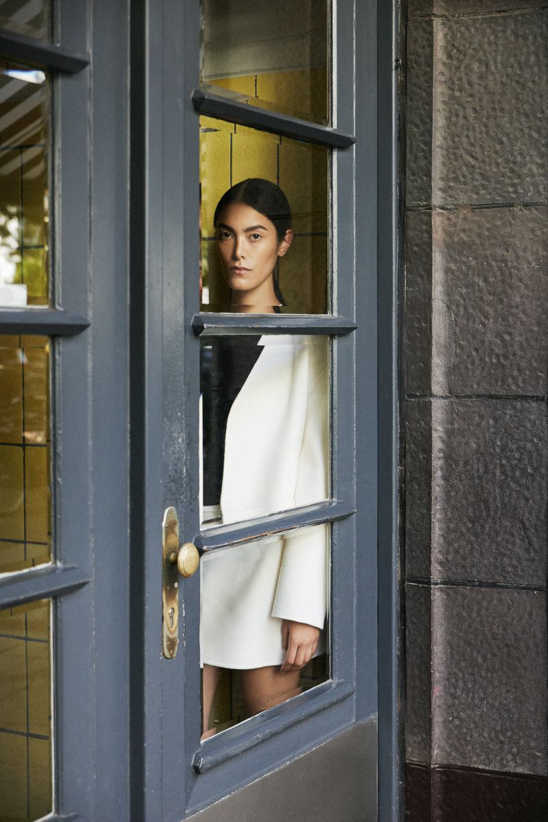 Fashion portrait of a woman with dark hair wearing a black and white dress, framed by a blue door with glass panes.
