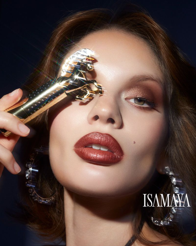 Beauty shot of a woman with makeup and jewelry holding a crystal-adorned beauty roller in a studio setting with dark background.