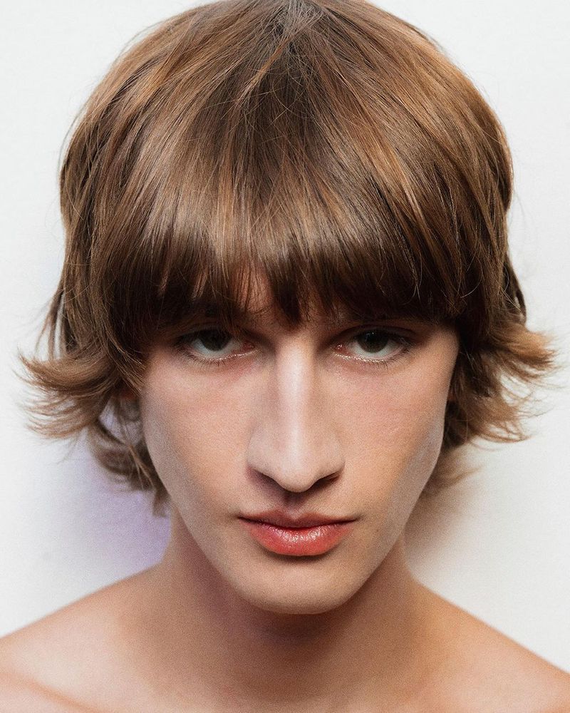 Close-up portrait of a model with layered brown hair and fringe against a neutral white background.