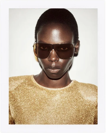Model wearing gold metallic top and dark sunglasses against a plain background