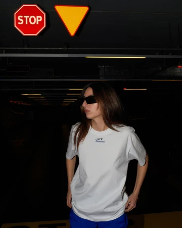 Stylish woman in sunglasses and casual clothing stands in a dark parking garage, with overhead traffic signs creating a unique composition.