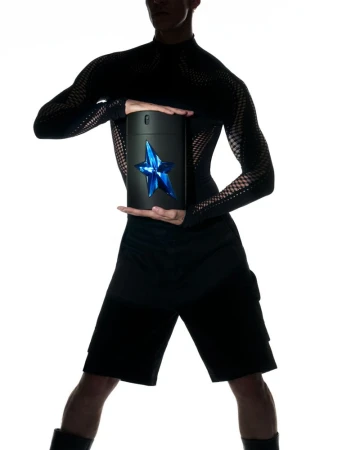 Black cylindrical bottle with blue star logo in the hands of a slim adult male in a black mesh shirt, silhouetted against a white background.