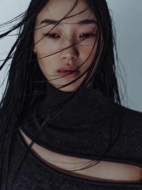 Close-up studio shot of an Asian adult female model wearing a grey turtleneck sweater with a cut-out neckline, set against a grey background.