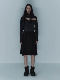 Model with long dark hair wearing a dark cut-out sweater and black skirt against a pale background