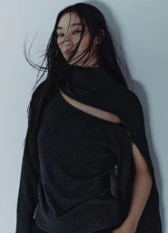 Asian woman with long dark windblown hair wearing a charcoal grey turtleneck sweater against a pale background