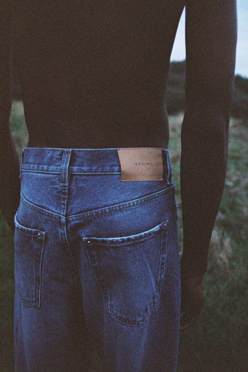 Close-up of a shirtless black man wearing blue denim jeans with a tan leather patch outdoors.