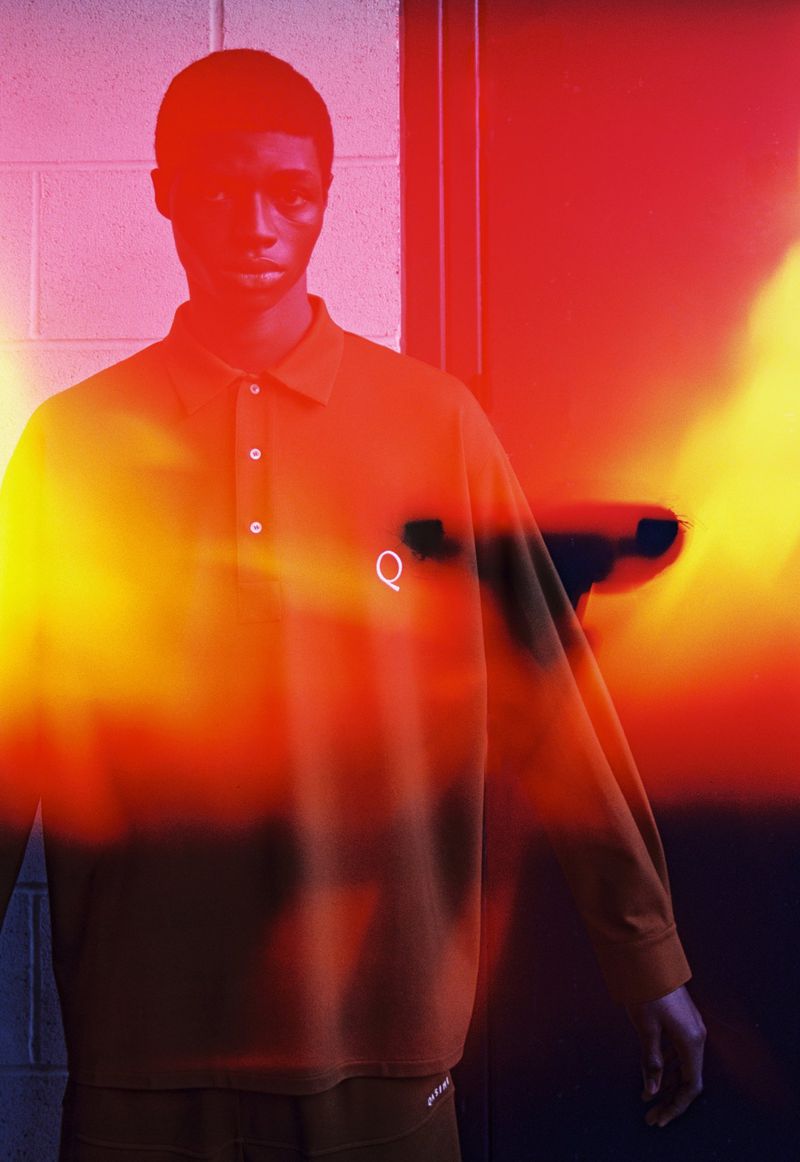 Indoor studio shot of a Black male model wearing a long-sleeve shirt with a logo; the image features a red and yellow color overlay.