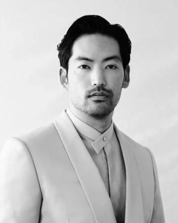 Black and white portrait of a handsome Asian man in an elegant suit, looking directly at the camera with a neutral expression.