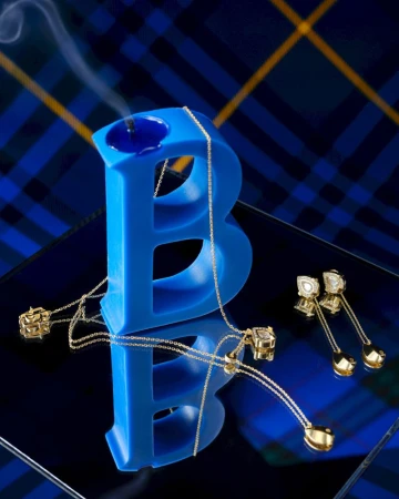 Elegant jewelry display featuring a blue letter 'B' candle holder, gold necklace, and drop earrings against a tartan backdrop.