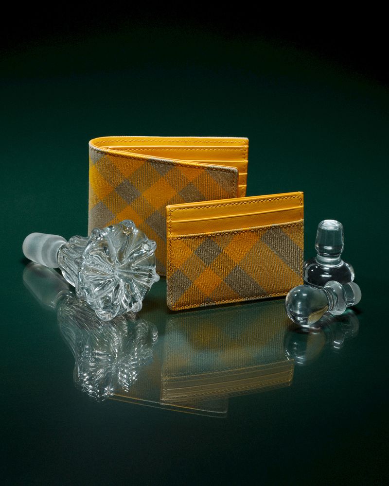 Wallet and cardholder set with a tan plaid pattern, displayed next to two crystal decanter stoppers on a reflective dark green surface.