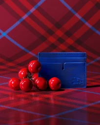 Royal blue leather cardholder beside a bunch of glossy red cherry tomatoes against a red tartan plaid backdrop.