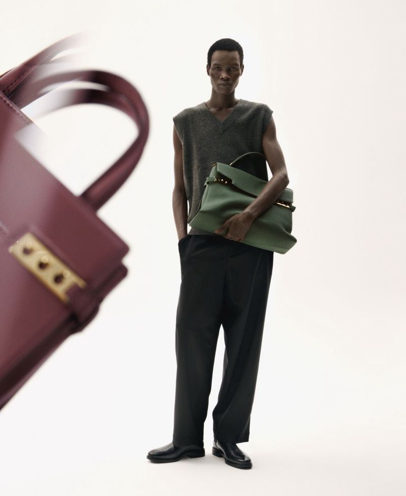 Full-length shot of a black male model with two leather bags on a white background, showcasing a minimalist fashion aesthetic.