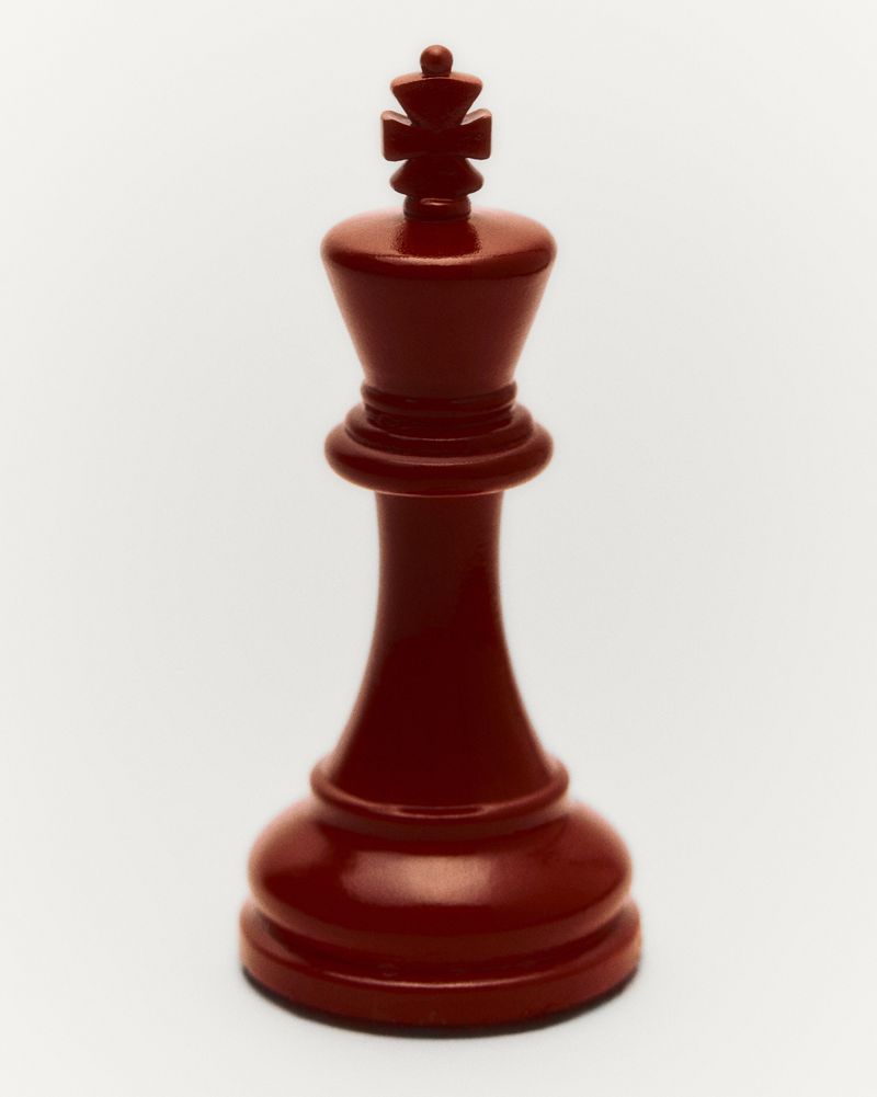 A red chess king piece is isolated against a plain background, showing its shape and design in a studio setting.