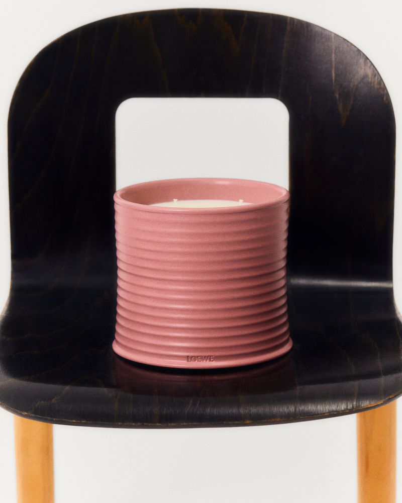 Dusty rose colored candle in a horizontally ribbed ceramic container sitting on a black chair against a white background.