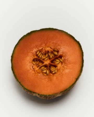 Studio shot of a halved cantaloupe melon on a white background showing the orange flesh and seeds in the center, simple food still life.