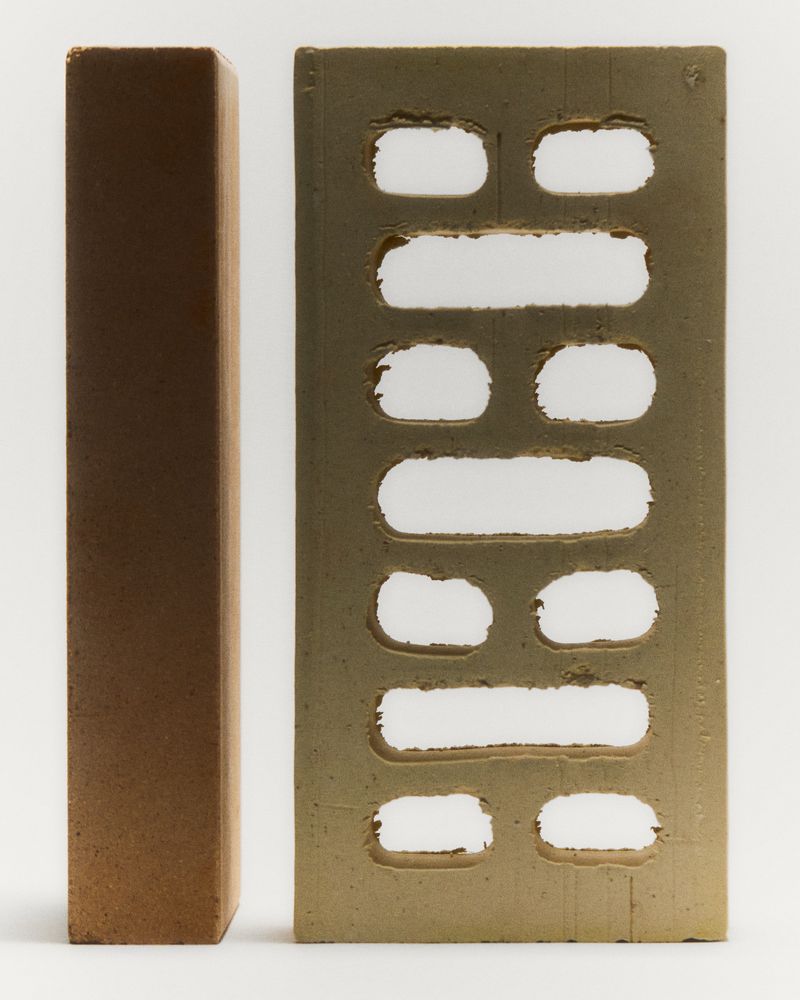 Two bricks are stacked against a plain white backdrop, one appearing to be solid and the other with a perforated rectangular design.