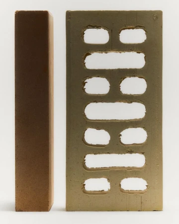 Two bricks are stacked against a plain white backdrop, one appearing to be solid and the other with a perforated rectangular design.