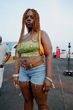 Stylish woman with braided hair, wearing a patterned top and denim shorts, poses confidently in an outdoor venue during daytime.