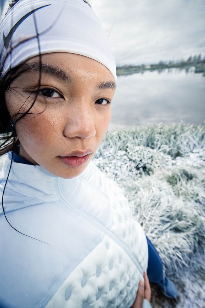 Close-up portrait of a woman wearing a white athletic headband and light blue winter jacket outdoors near a frozen lake.