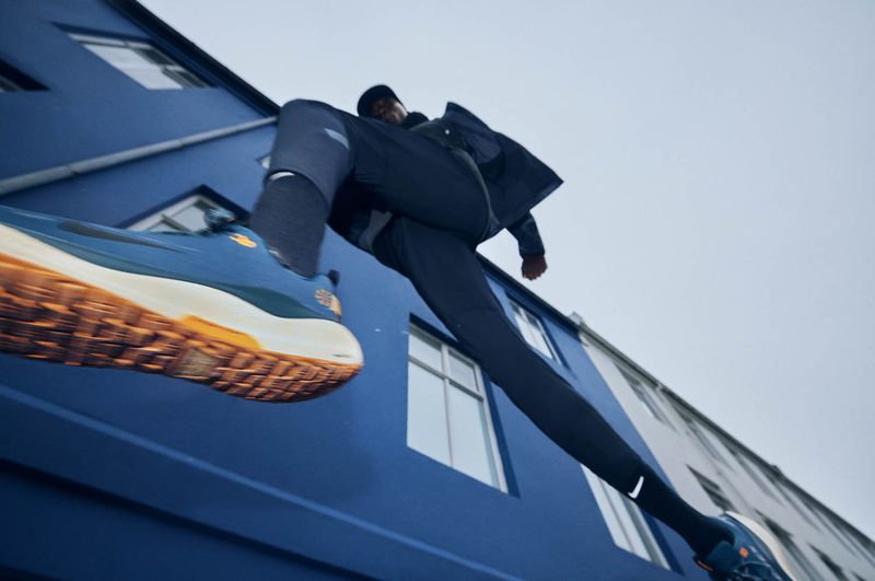 Low-angle shot of a person in activewear leaping against a bright blue building, highlighting the blue and orange sneakers in mid-air.