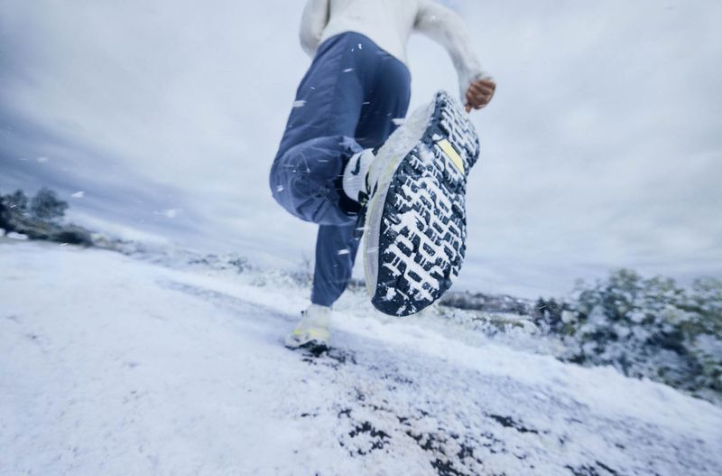 Close-up of a runner's shoe making contact with snow-covered ground, action shot emphasizing motion, athleticism, and winter fitness.
