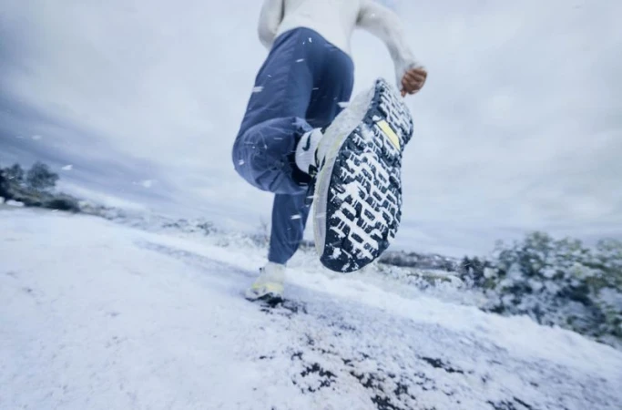 Close-up of a runner's shoe making contact with snow-covered ground, action shot emphasizing motion, athleticism, and winter fitness.