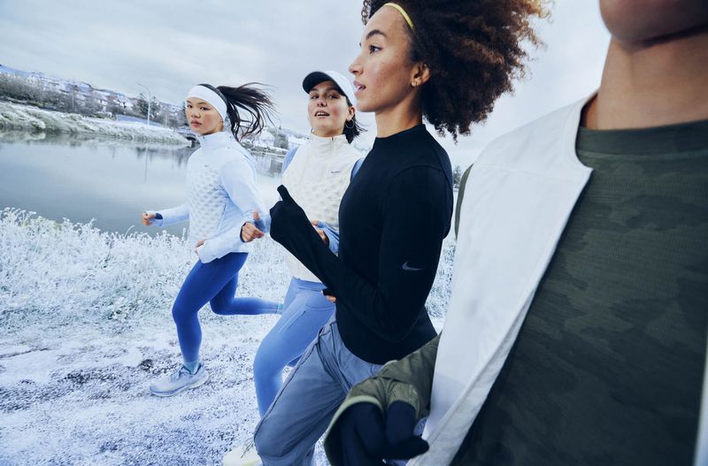 A group of athletes runs in a cool-toned, outdoor setting, wearing athletic attire, captured in medium shot near a body of water.