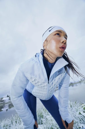 Portrait of a young Asian woman in athletic wear, outside near icy water, looking up toward the sky on a cold day.