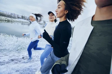 Group of runners in winter athletic apparel running along a snowy outdoor path near water photographed by Sophie Jones.