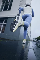 Low-angle action shot of a runner in blue leggings and sneakers running past a wet building exterior