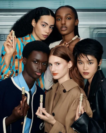 Five diverse models posing together while holding Gucci Beauty concealer tubes in front of a train carriage background.