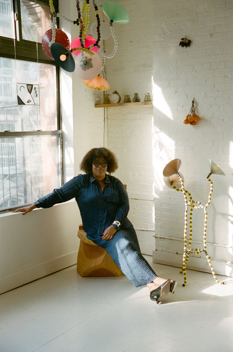 Woman in denim sitting next to a window with unique art installations in a brightly lit room with white walls and light floors.