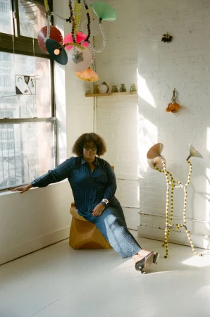Woman in denim sitting next to a window with unique art installations in a brightly lit room with white walls and light floors.