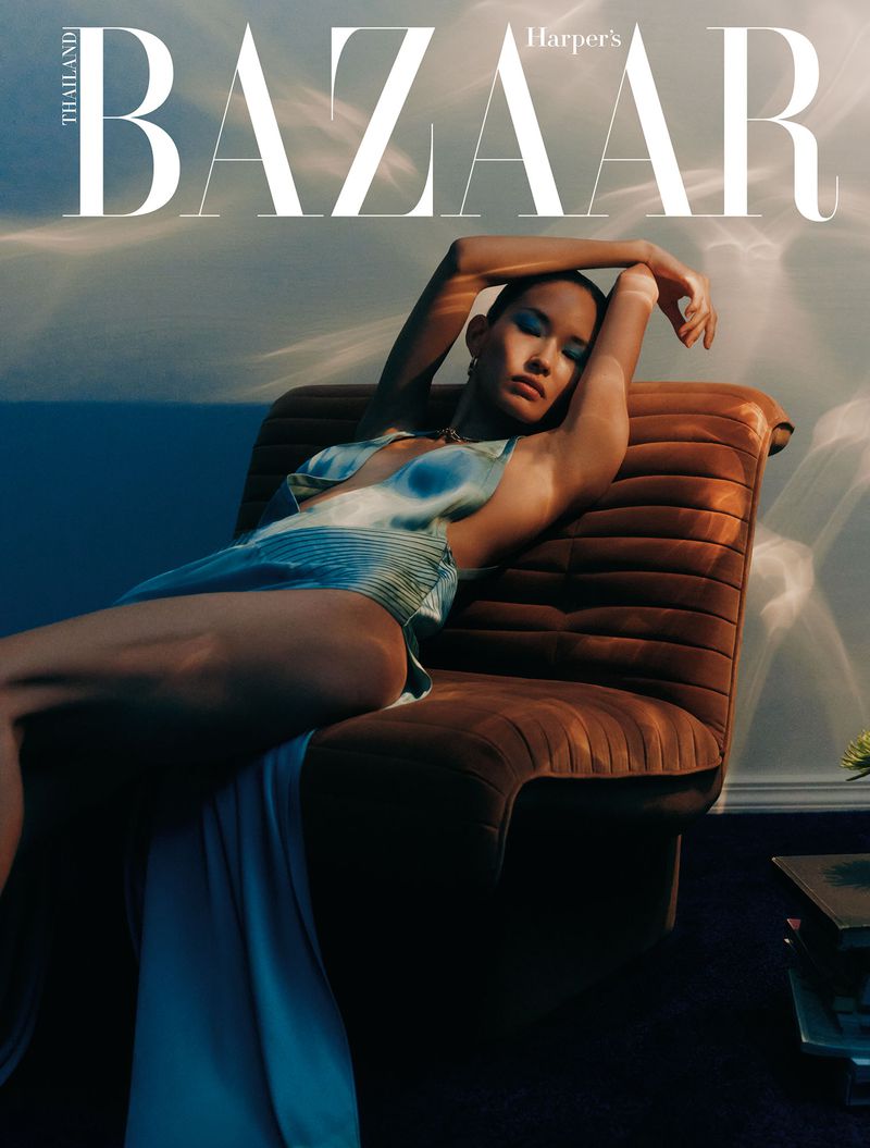 Woman in tie-dye swimwear lounges on a brown chair against a blurred sky backdrop, posing for a Harper's Bazaar Thailand cover.