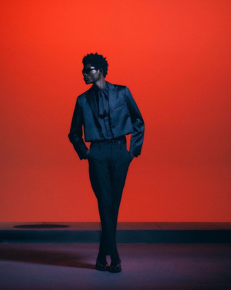 Fashionable Black male model in a dark suit posing in a photo studio with a bright red background and dramatic lighting, full body shot.